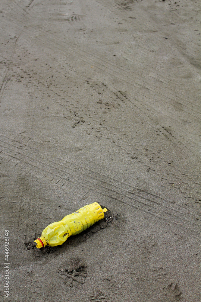A yellow plastic bottle on the sand on the beach making pollution, the trash on the beach