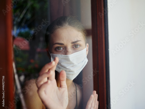 woman in medical mask looking out the window lockdown close-up