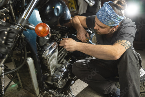 Confident, in bondana, young man in a repair shop, sitting in front of a retro motorcycle. Auto mechanic, portrait. photo