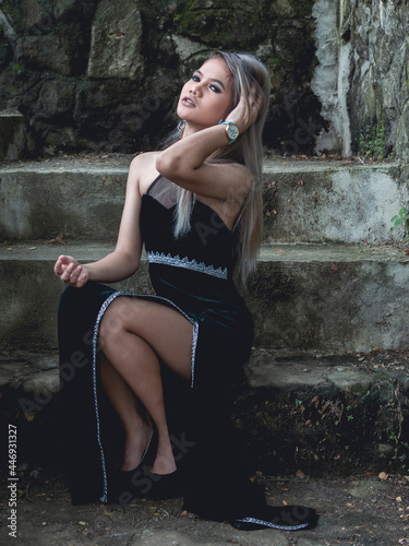 Obraz na plátně A beautiful and elegant young asian woman in an elegant black dress sitting in moss covered stairs