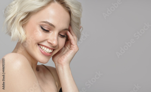 Portrait of a beautiful smiling blonde girl with a short haircut. Gray background.