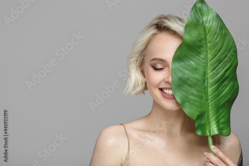 Portrait of blonde woman and green leaf. Organic cosmetics concept. Gray background.