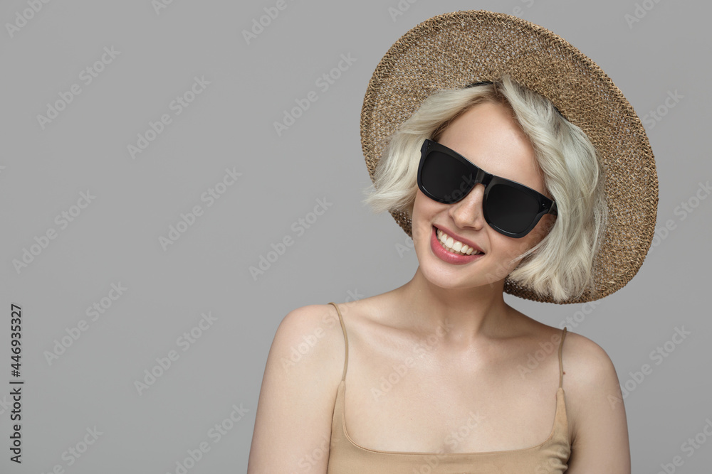 Smiling girl with a short haircut in a hat and sunglasses. Grey background.