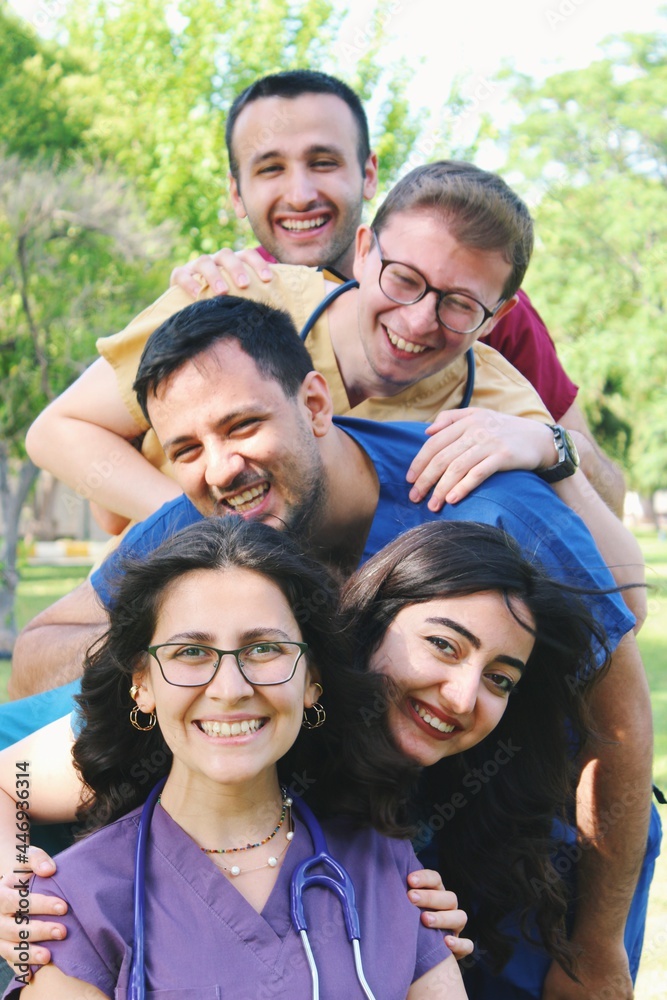 Five friends / medicine students / healthcare workers / intern doctors & scrubs happy portrait outdoors in hospital courtyard Five friends / medicine students / healthcare workers / intern doctors & scrubs happy portrait outdoors in hospital courtyard