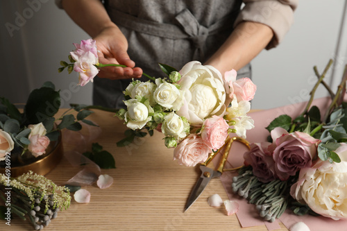 Florist creating beautiful bouquet at wooden table indoors, closeup photo