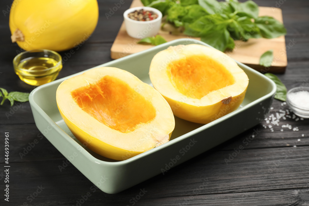 Raw spaghetti squash halves in baking dish and spices on dark wooden table Raw spaghetti squash halves in baking dish and spices on dark wooden table