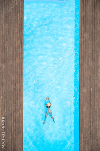 Young alone beautiful sports woman in bikini and hat is swimming in swimming pool. Aerial drone view from above. Tropical summer vacation