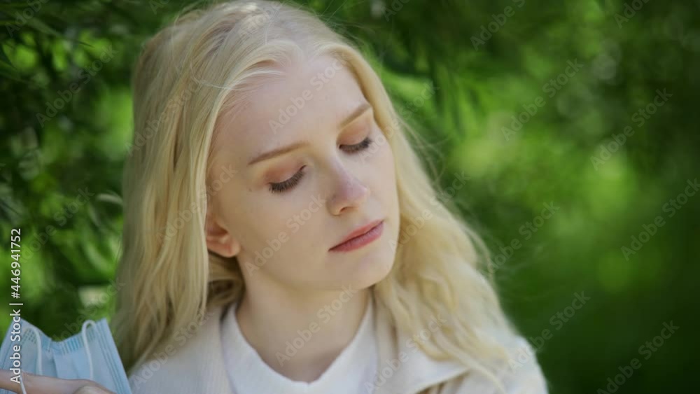 Beautiful blonde woman takes off the medical mask and sniffs the flower. She enjoys the fresh air and the scent of dandelion. Close-up, 4K UHD. Beautiful blonde woman takes off the medical mask and sniffs the flower. She enjoys the fresh air and the scent of dandelion. Close-up, 4K UHD.