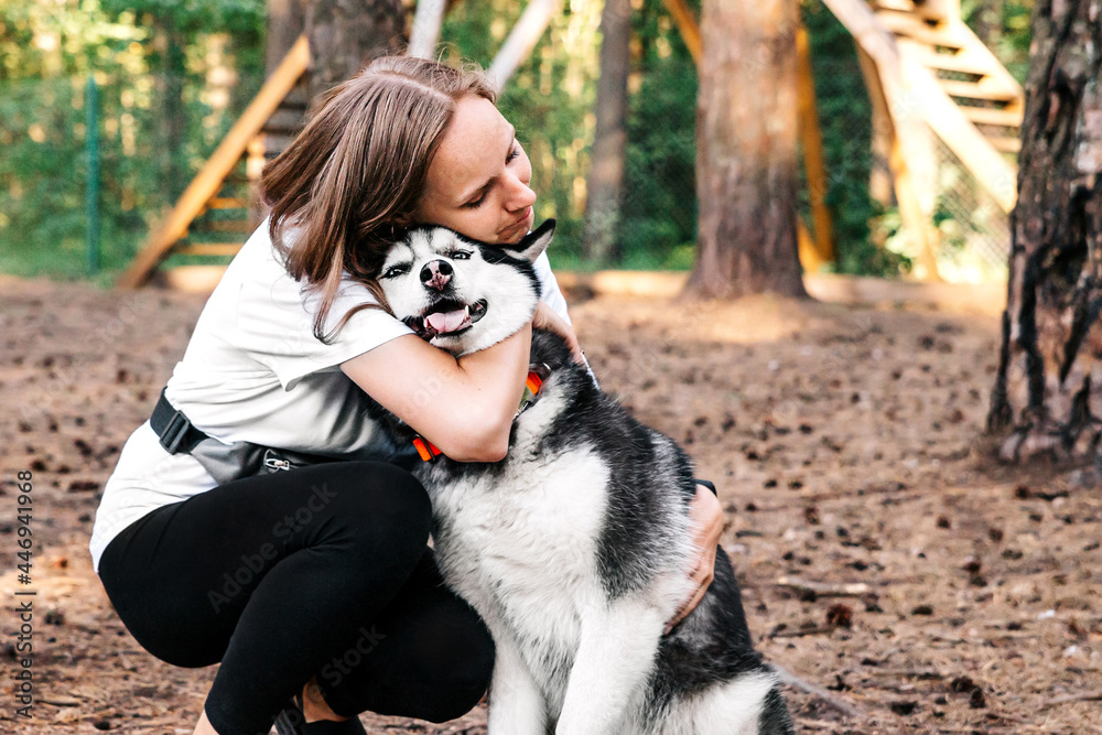 A woman with all her love hugs a husky dog. Husky stuck out her tongue with pleasure, the friendship of man and animal. Dog training on the playground. A pet on a walk A woman with all her love hugs a husky dog. Husky stuck out her tongue with pleasure, the friendship of man and animal. Dog training on the playground. A pet on a walk