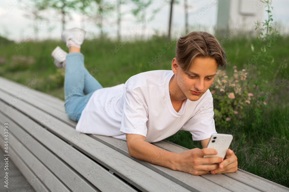 Fototapeta premium young guy lies on a bench with a mobile phone 