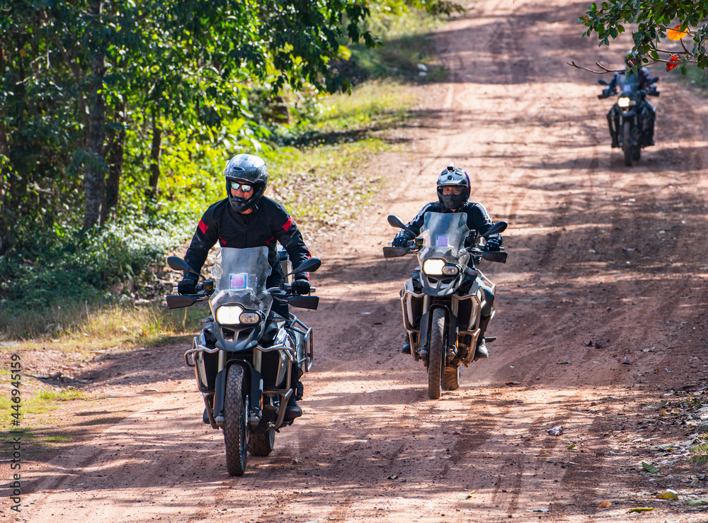 Men riding their adventure motorbikes on dusty road in Cambodia Men riding their adventure motorbikes on dusty road in Cambodia