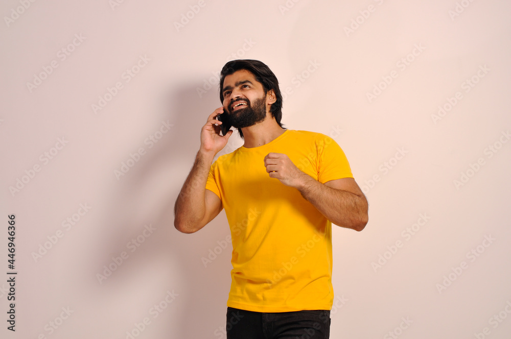 Young Indian man wearing yellow t-shirt Talking on a mobile phone and smiling 