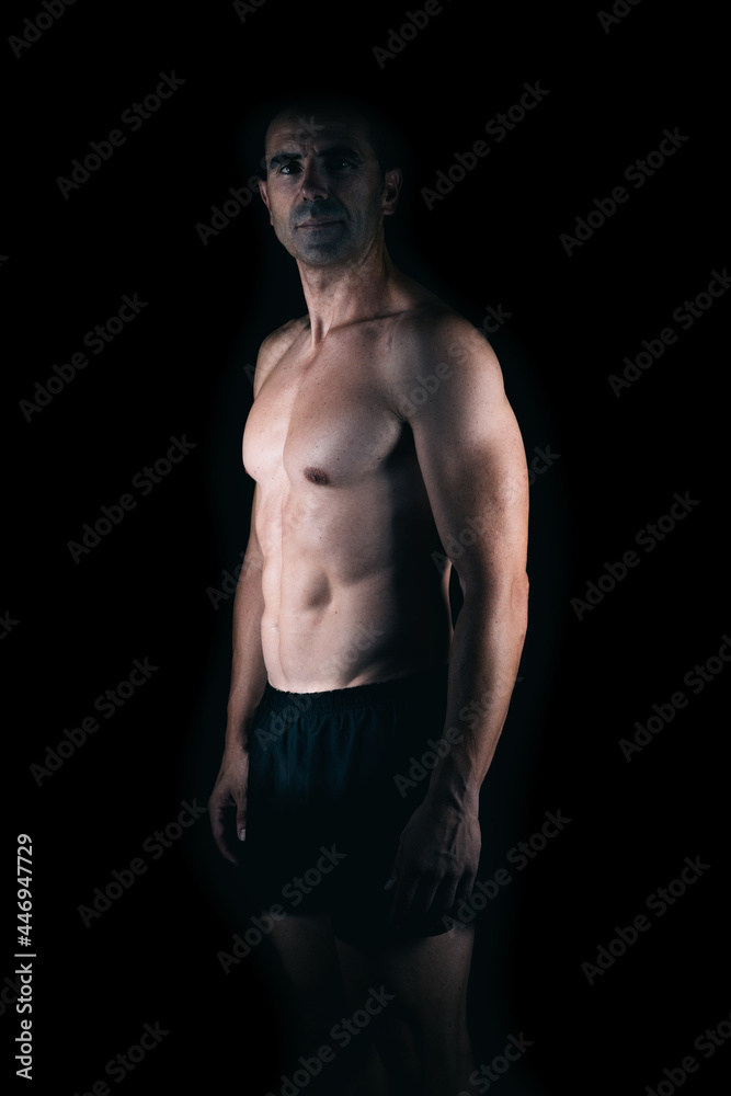 Strong man facing the camera while the light lighting his torso Strong man facing the camera while the light lighting his torso