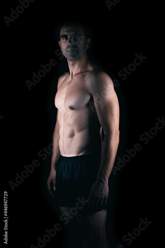 Strong man facing the camera while the light lighting his torso