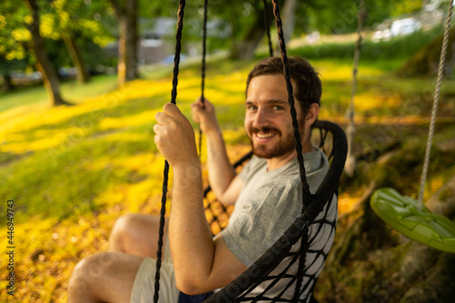 Photo of a attractive young guy relaxing on a hammock in the middle of nature. It is a summer day in the forest and he has a happy smile
