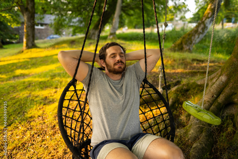 Photo of a attractive young guy relaxing on a hammock in the middle of nature. It is a summer day in the forest and he has a happy smile