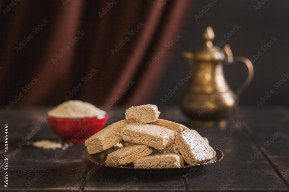 Pieces of tahini halva, sesame seeds in a bowl, an vintage jug.