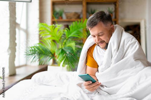 Middle aged man in bed checking his messages in smartphone after awakening. Addiction to social networks concept.