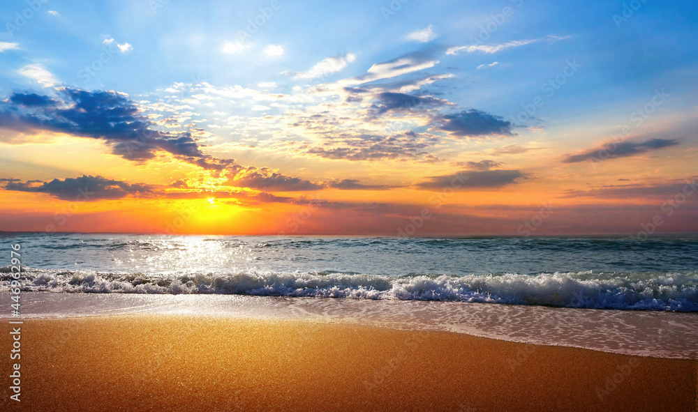 Beautiful natural seascape with colorful sunset sky. Waves of sea surf and golden sand of beach in rays of sunlight.