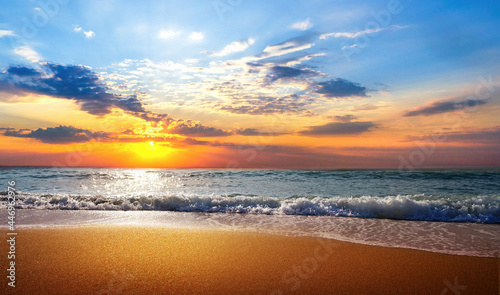 Beautiful natural seascape with colorful sunset sky. Waves of sea surf and golden sand of beach in rays of sunlight.