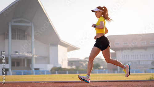 A young Asian woman athlete runner jogging on running track in city stadium in the sunny morning to keep fitness and healthy lifestyle. Young fitness woman runs on stadium track. Sport and recreation