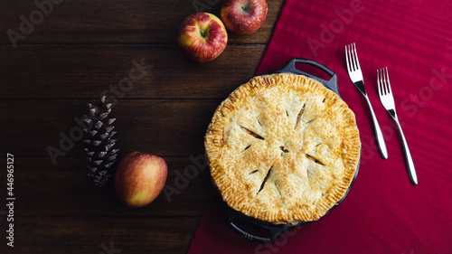 American apple pie on wooden table. Arranged with apples, pinecone and red table runner.