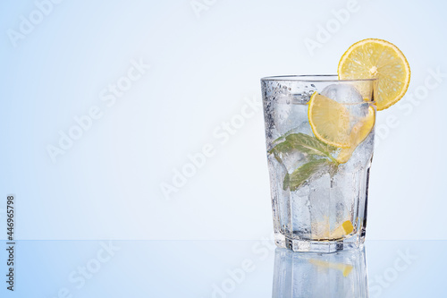 Glass of water with fresh lemons, leaves of mint and ice cubes on blue background. Refreshing lemonade, lemon drink.