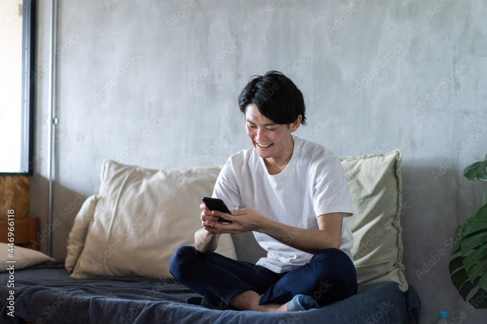 一人暮らしの家でスマホを使う若い男性 一人暮らしの家でスマホを使う若い男性