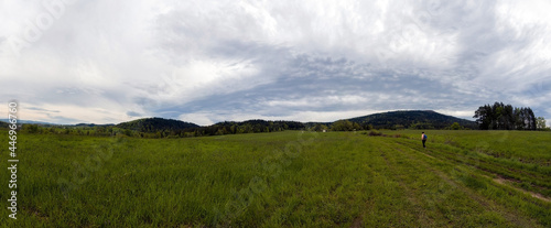Rabka Zdroj, Poland : Panorama view of a person with backpack hiking or walking in a middle of a meadow field in country side against hills near rabka on a way to lubon wielki