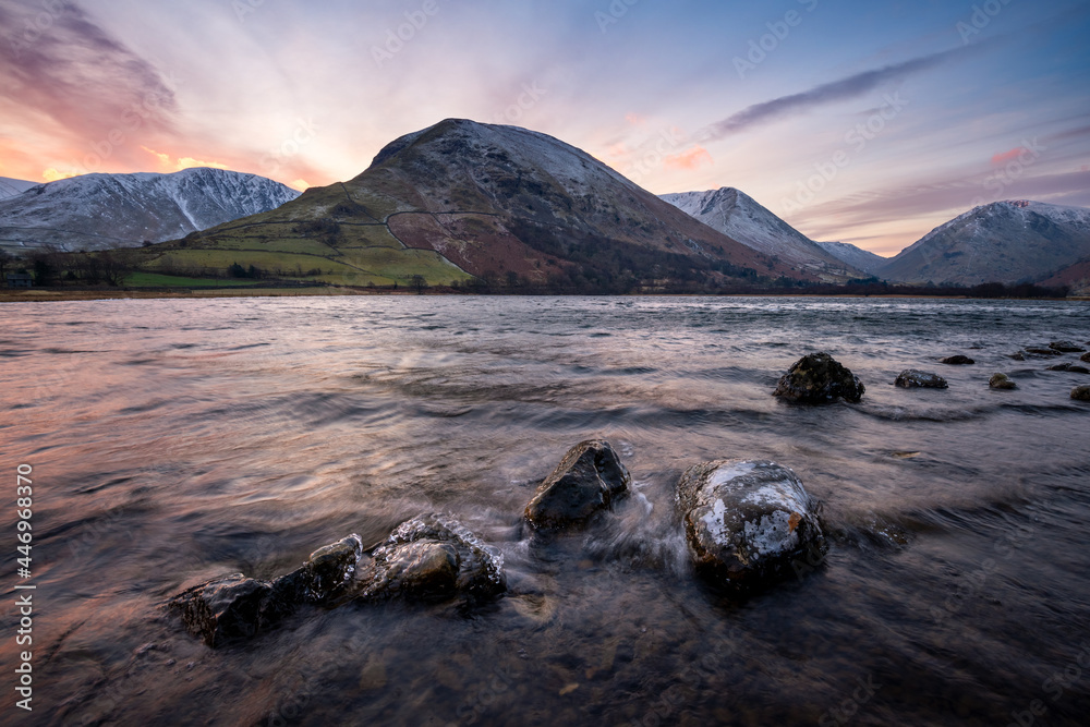 Snowcapped mountains at sunrise seen from lake shoreline. Lake District, UK.