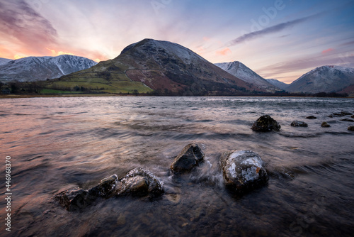 Snowcapped mountains at sunrise seen from lake shoreline. Lake District, UK.