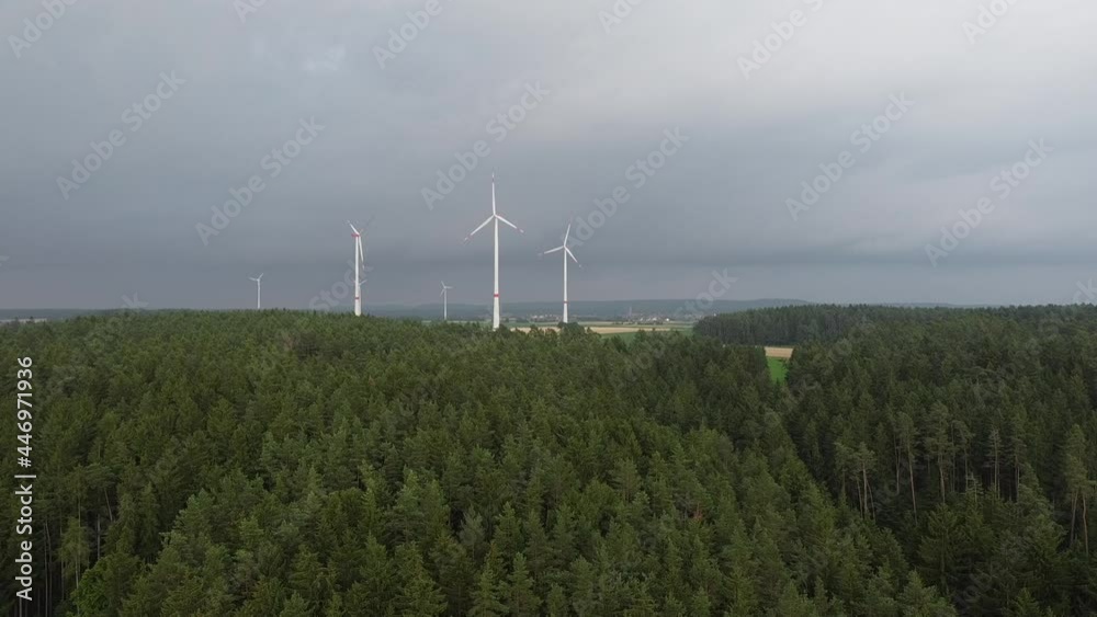 On a mountaintop surrounded by pine forest, wind turbines churn away in the distance. On a mountaintop surrounded by pine forest, wind turbines churn away in the distance.