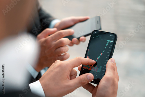 Growth charts on stock markets. Male brokers hold phones in their hands. Cryptocurrency trading on the stock exchange