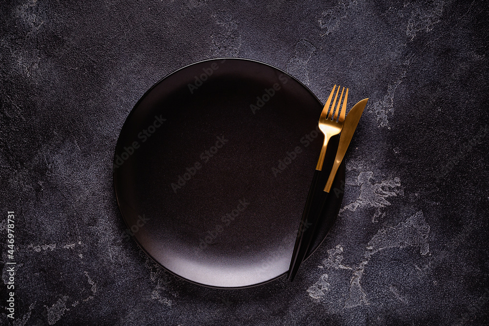 Clean empty black plate with cutlery.