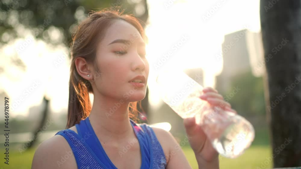 A woman is drinking water beside a pond in the city park 