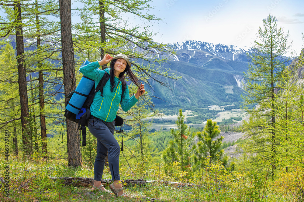 Woman is a happy beautiful tourist with a backpack on a hike against the background of mountains and trees