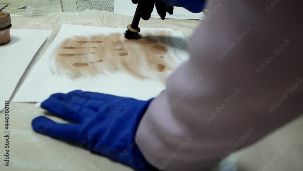 A crime scene investigator dusts for fingerprints with a forensic brush to solve a mystery. Dusting For Fingerprint Evidence. Criminologist police chemist takes palm prints from a sheet of paper.
