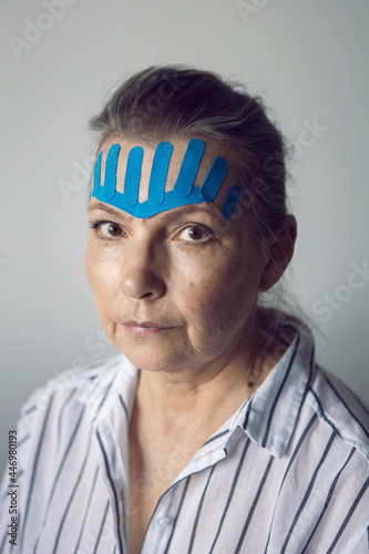 gray-haired elderly woman with kinesiotaping on her face to smooth out wrinkles photo