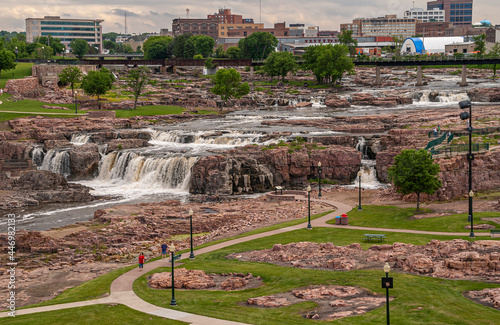 Sioux Falls, SD, USA - June 2, 2008: Looking over a section of teh water cascades with part of city skyline in back. Brown rocks and foaming water, with some green foliage sprinkled around. 