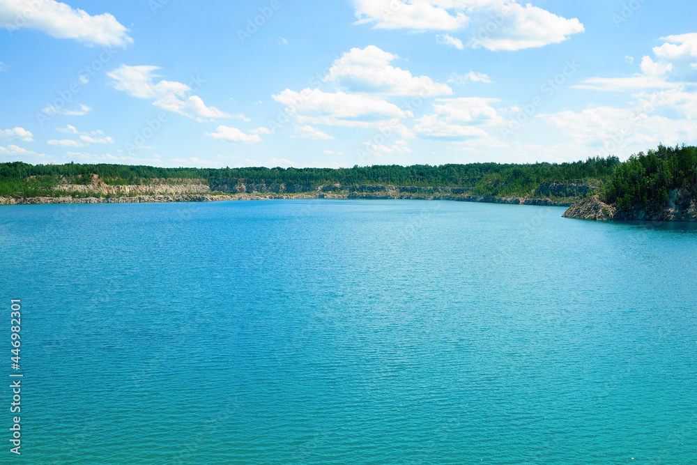 A clear blue lake under a blue sky, surrounded by rocks with a forest. Serene water surface A clear blue lake under a blue sky, surrounded by rocks with a forest. Serene water surface