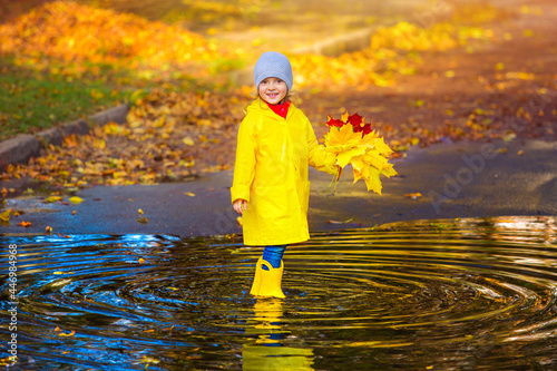 Fototapeta Naklejka Na Ścianę i Meble -  a happy girl child in a yellow raincoat and rubber boots in a puddle on an autumn walk