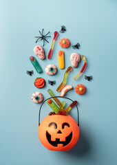 Various halloween sweets and candies in a pumpkin pot top view on blue solid background