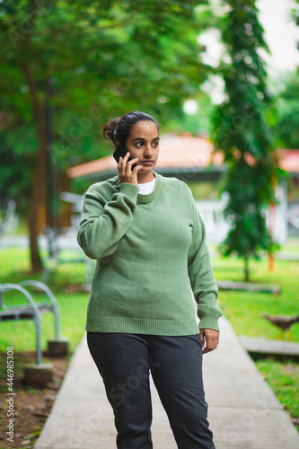 young latin woman walking in the park while talking on the phone