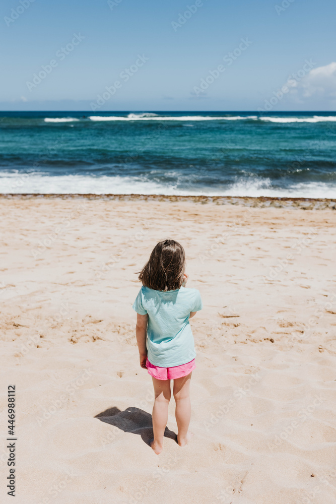Young girl watches ocean waves from a beach in Oahu Young girl watches ocean waves from a beach in Oahu