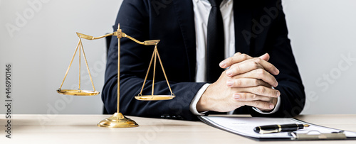 A male lawyer sits in the office of his law firm, on a table with a scale of justice and a hammer laying down, he is an attorney serving his client. Lawyer concepts and lawful justice. photo