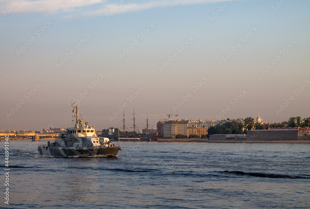 St. PETERSBURG, RUSSIA-JULY, 15, 2021: a warship sailing along the Neva River at dawn against the background of the embankment and historical architecture in the early summer morning St. PETERSBURG, RUSSIA-JULY, 15, 2021: a warship sailing along the Neva River at dawn against the background of the embankment and historical architecture in the early summer morning