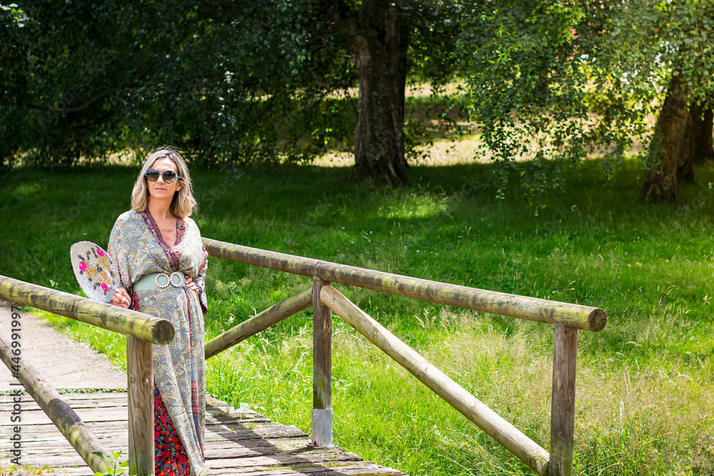 Naklejka premium Blonde woman posing in a long dress on a wooden bridge in a park in Asturias, Spain.The photograph is taken in horizontal format.