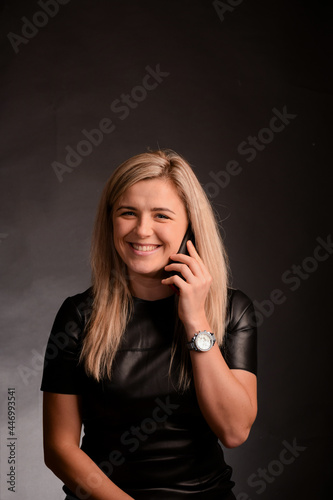 Attractive blonde girl cute smiling and talking on a mobile phone on a dark background in the studio.