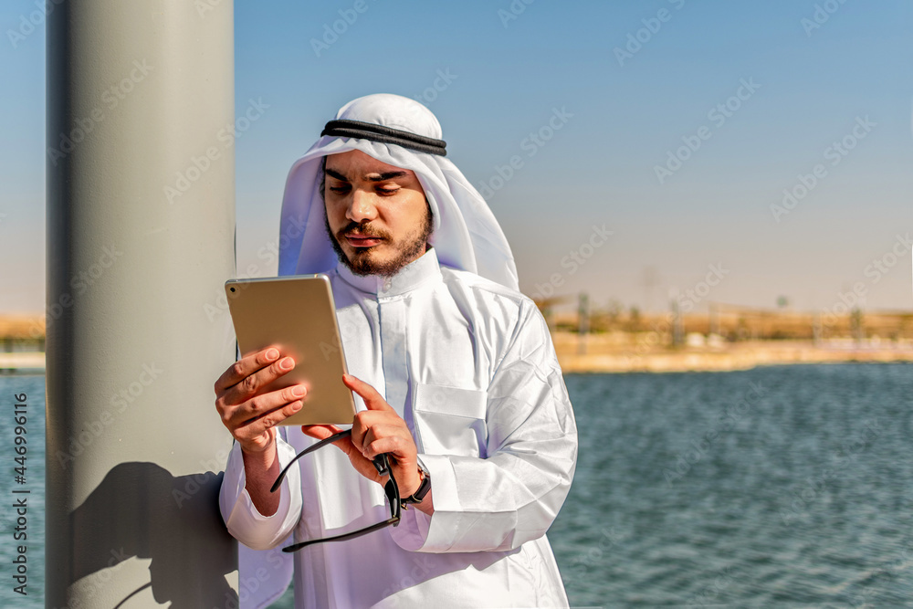 Portrait of a concentrated Islamic man, in traditional clothing, checking content on a tablet, in the Middle East. Portrait of a concentrated Islamic man, in traditional clothing, checking content on a tablet, in the Middle East.