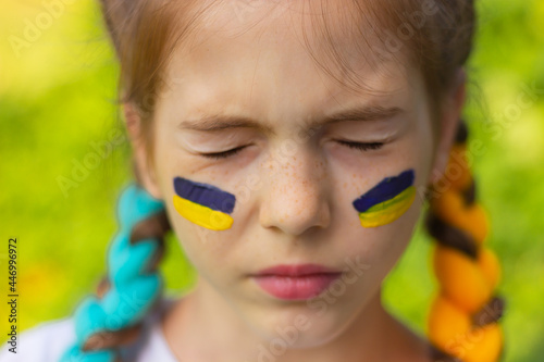 the face of a girl with closed eyes and with yellow-blue national flags of Ukraine painted on her cheeks. concept of Ukrainian patriotism  independence day. sports and fan support.